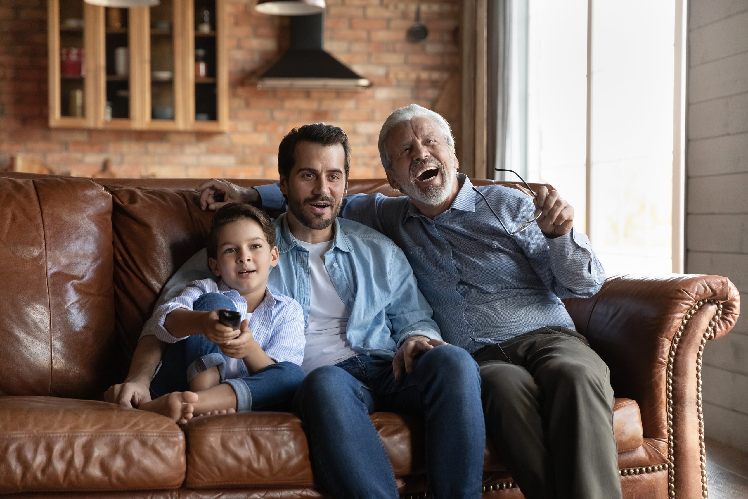 Three male members of multi generational family watching tv together