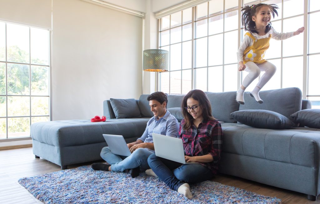 Girl jumping on sofa while mom and dad working at home.