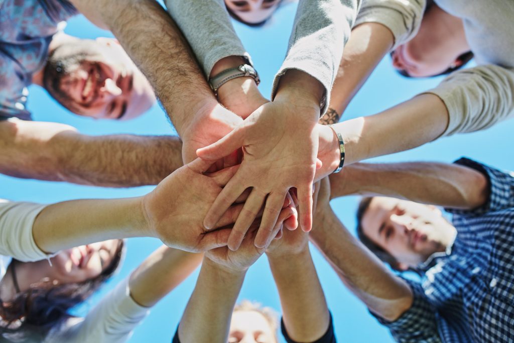 Low angle shot of a group of people joining their hands together in unity outdoors